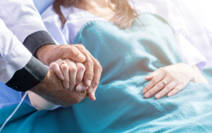 Doctor sosteniendo la mano de una paciente en consulta oncológica, simbolizando empatía y apoyo en el tratamiento de leucemias o cáncer hematológico.