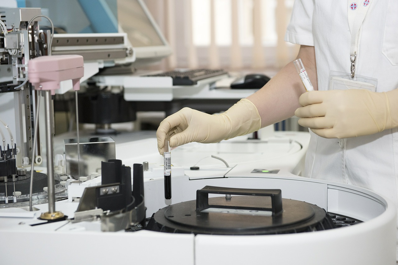 Técnico de laboratorio con guantes sostiene tubo de ensayo en un laboratorio clínico, rodeado de equipo médico especializado.